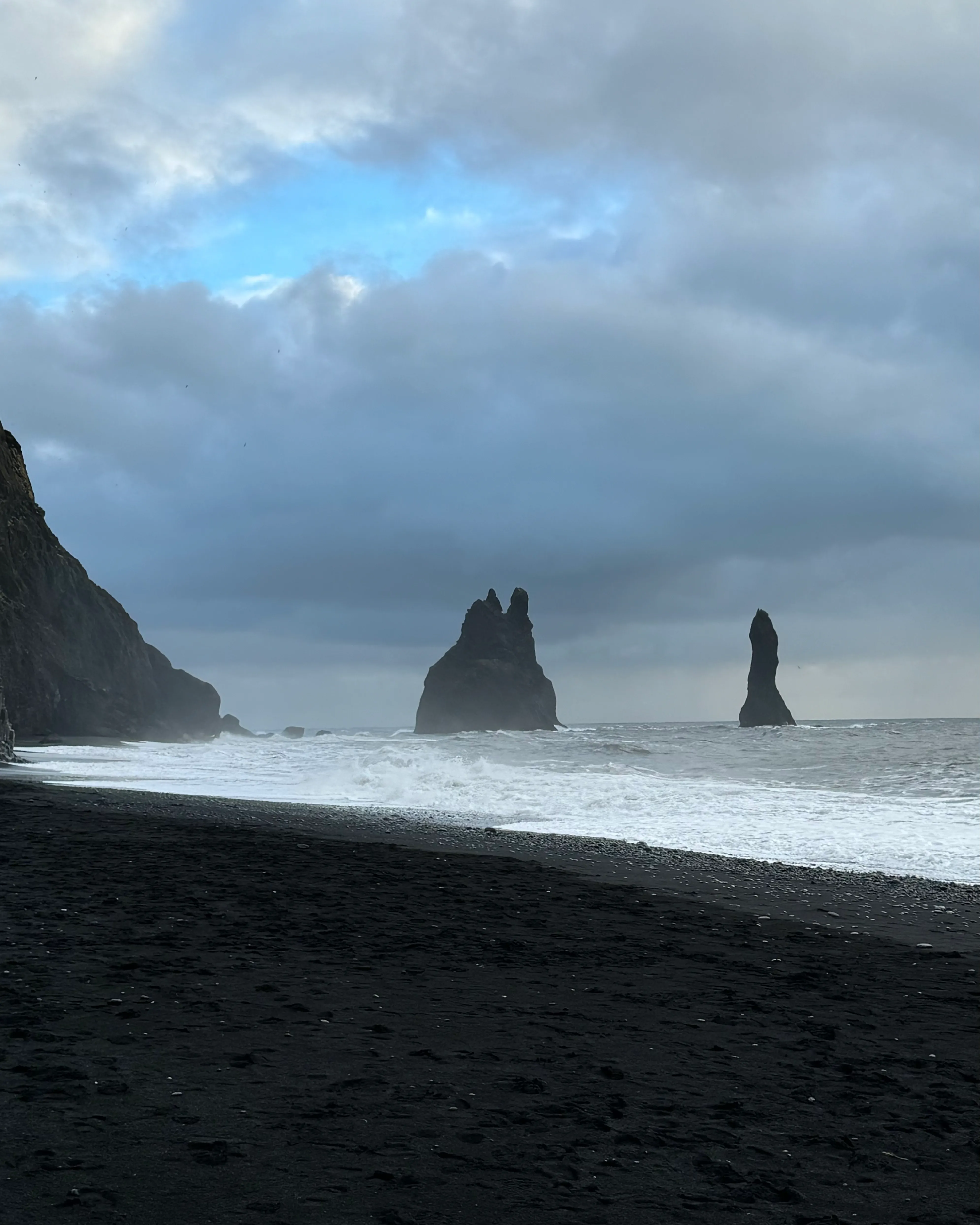 Towers of rock formations in the water from a black sand beach