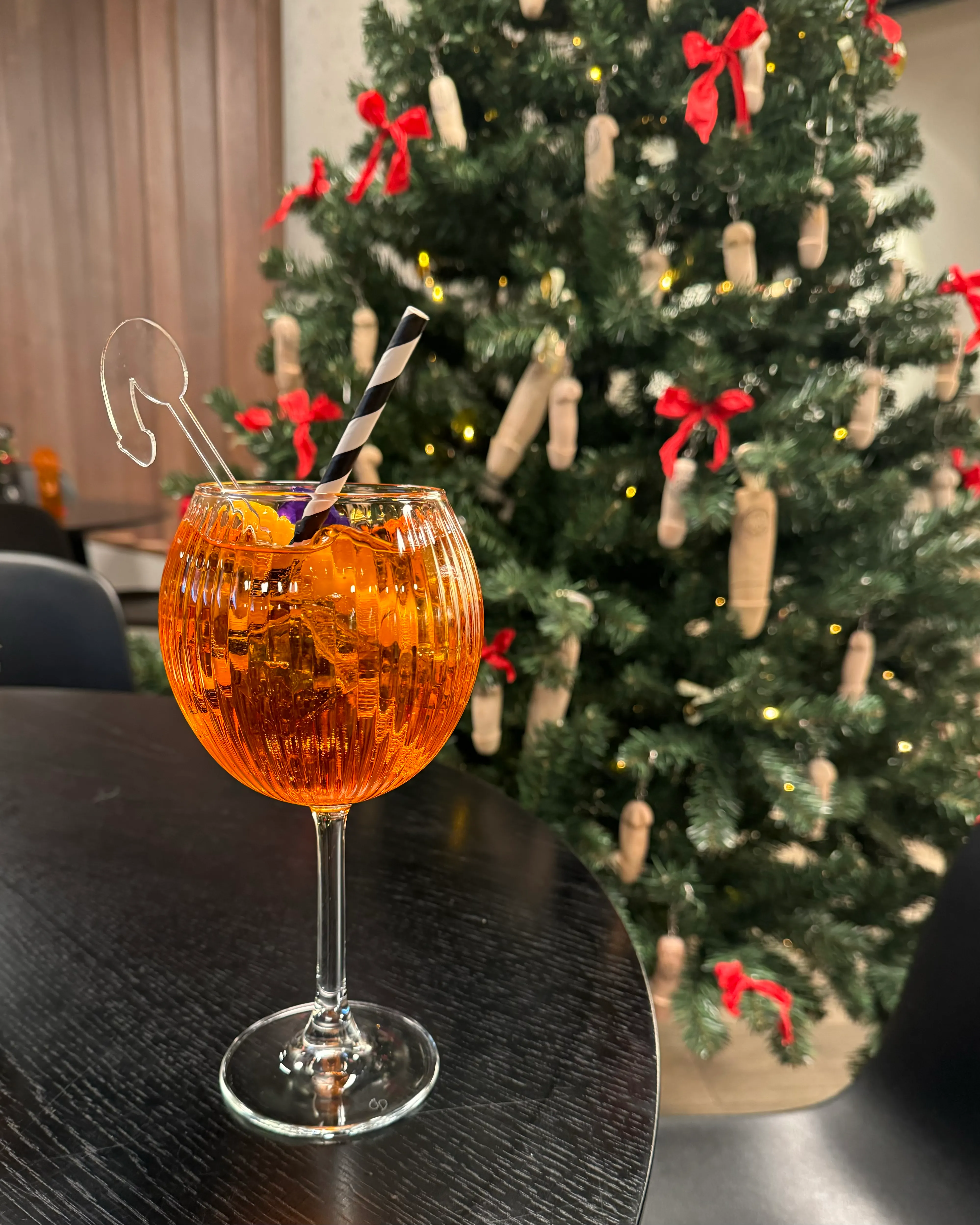 An Aperol Spritz COCKtail in front of a tree decorated with penis keychains instead of ornaments